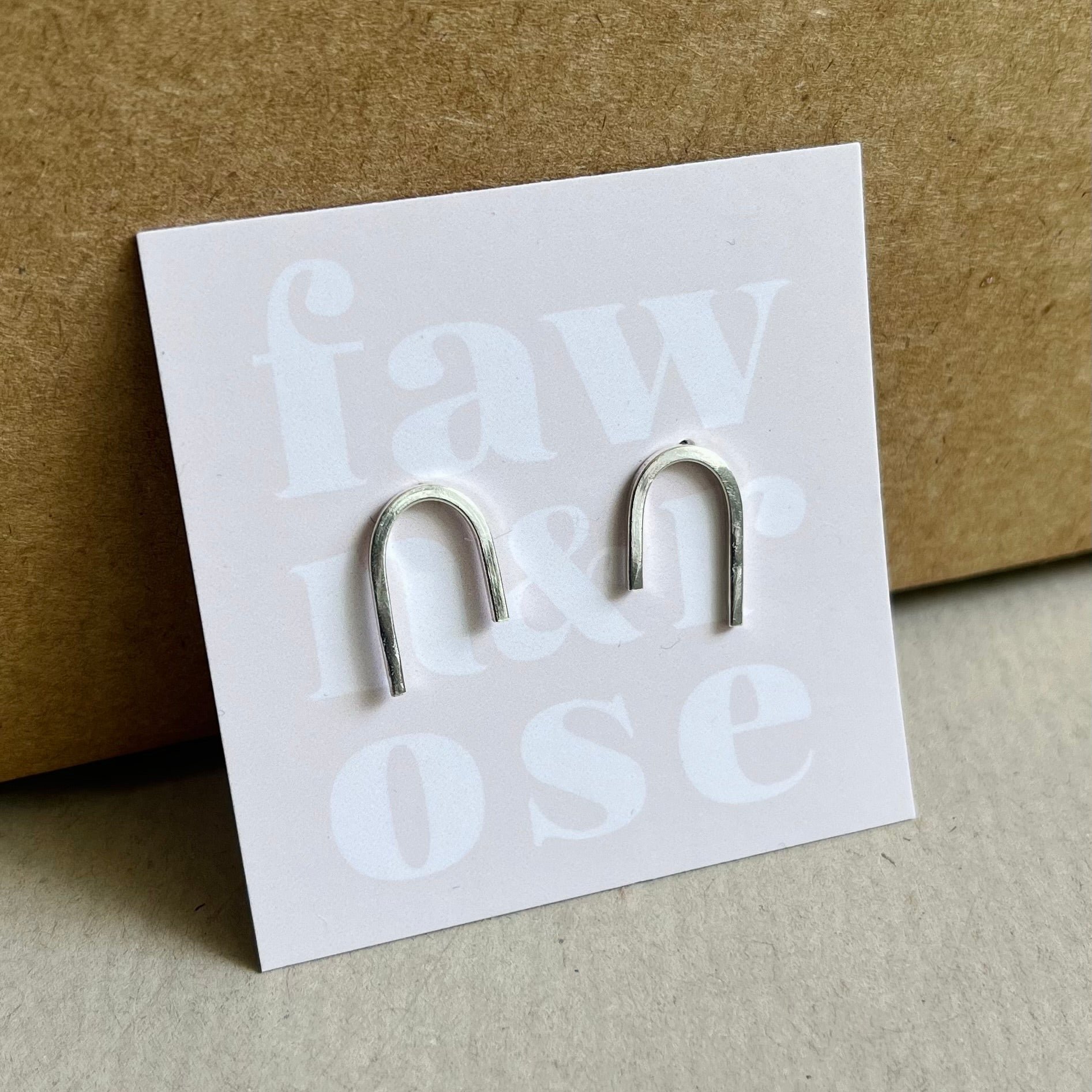 Silver arc minimalist earrings on soft pink card wiht words fawn and rose in white text