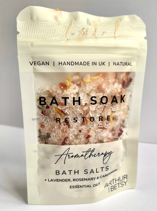 Beige pouch of luxury bath salts which are pink in colour and the pouch has the words bath soak restore on it.