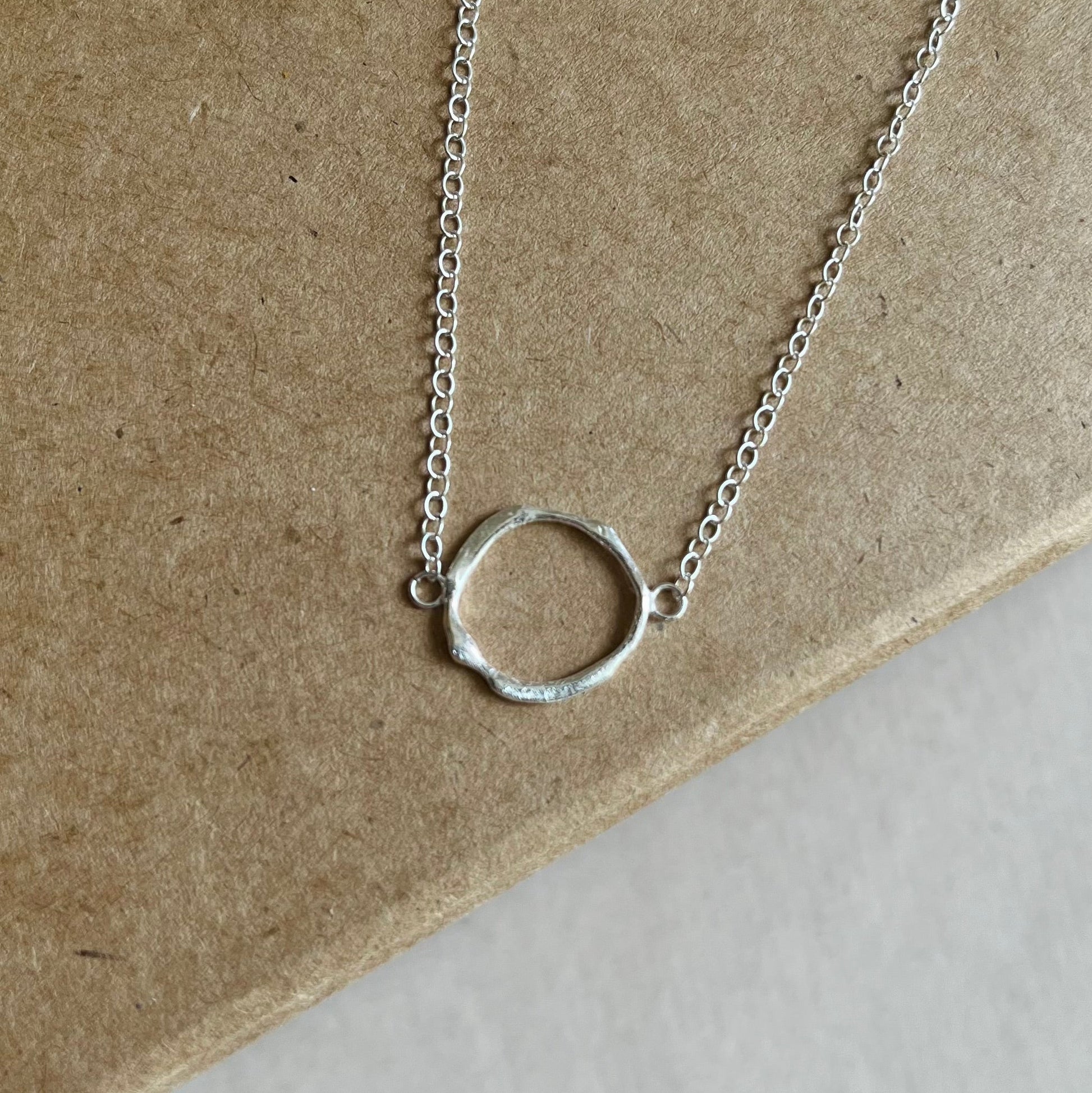 Close up of silver circle necklace on top of a Kraft gift box