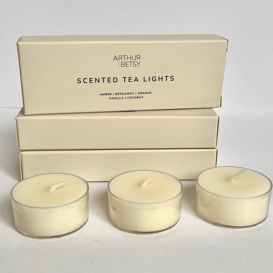 Three scented tea lights shown in front of three stacked beige boxes with the wording scented tea lights on the box