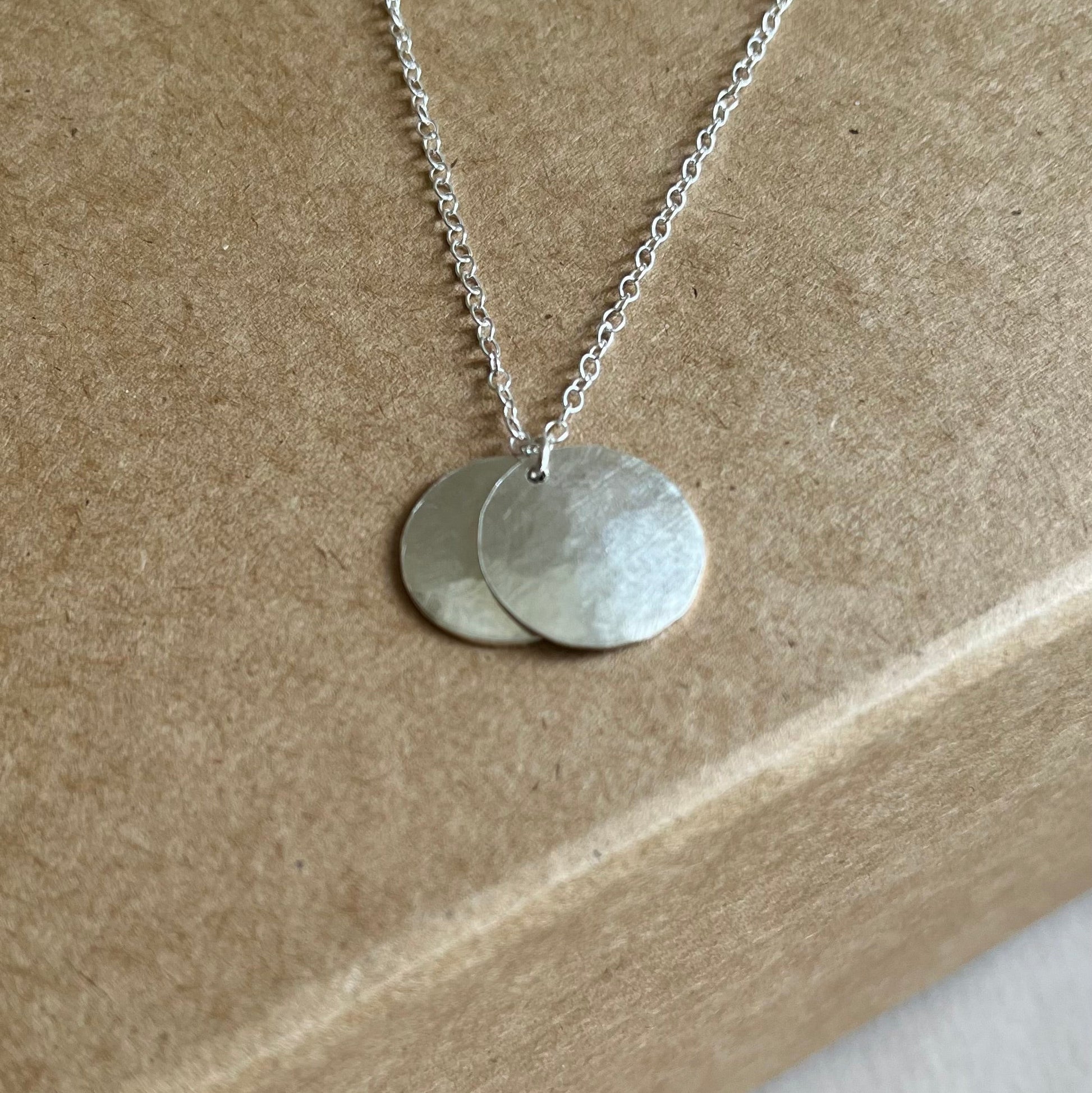 Close up image of silver double disk necklace on silver chain shown on a Kraft gift box.