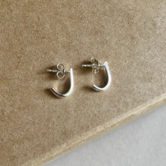 A pair of sterling silver wraparound stud earrings placed on a cardboard surface.