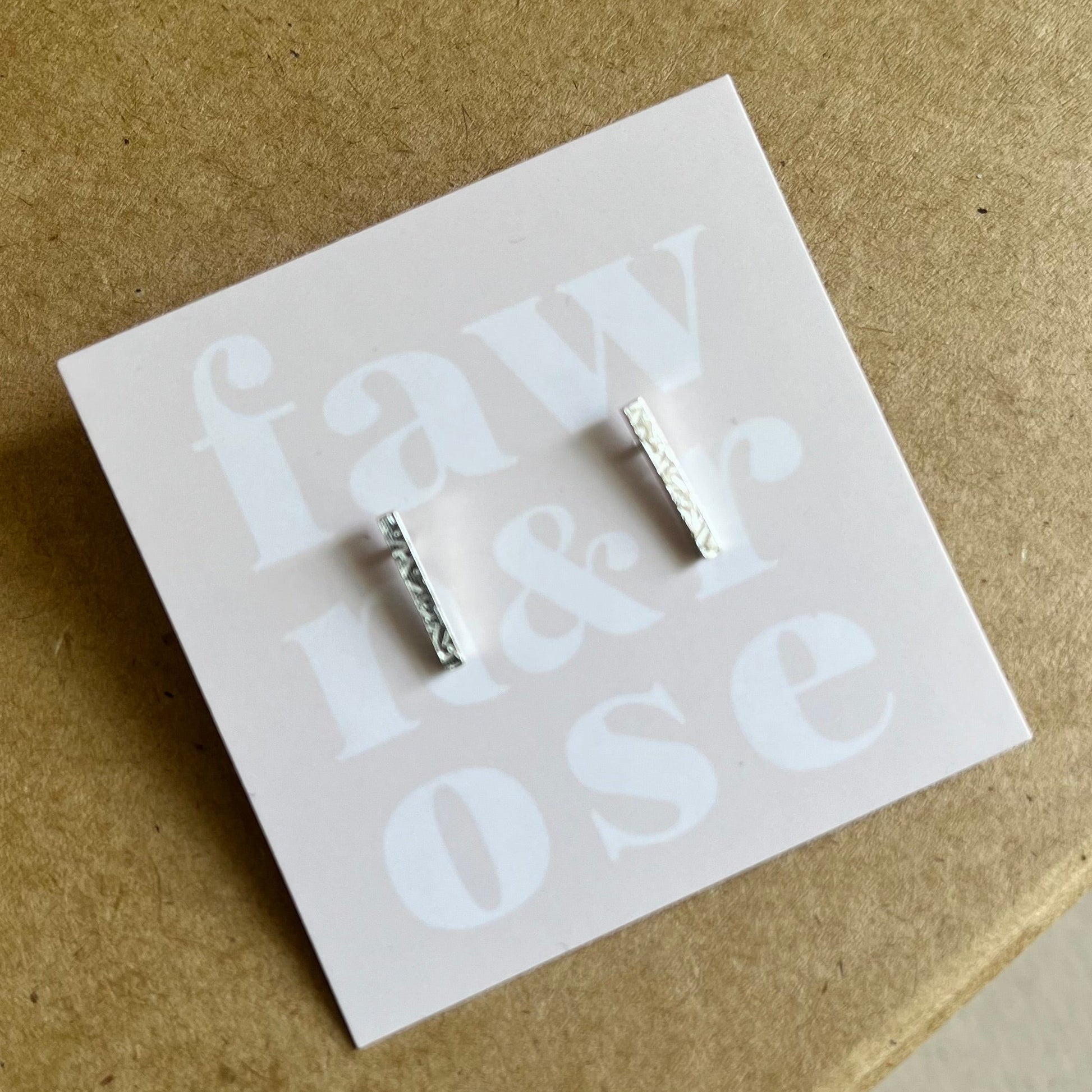 Close up of silver bar studs on blush pink card shown on a Kraft gift box