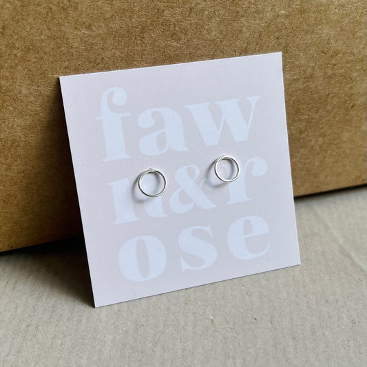 Tiny open circle stud earrings on soft pink card packaging with the words fawn and rose on.