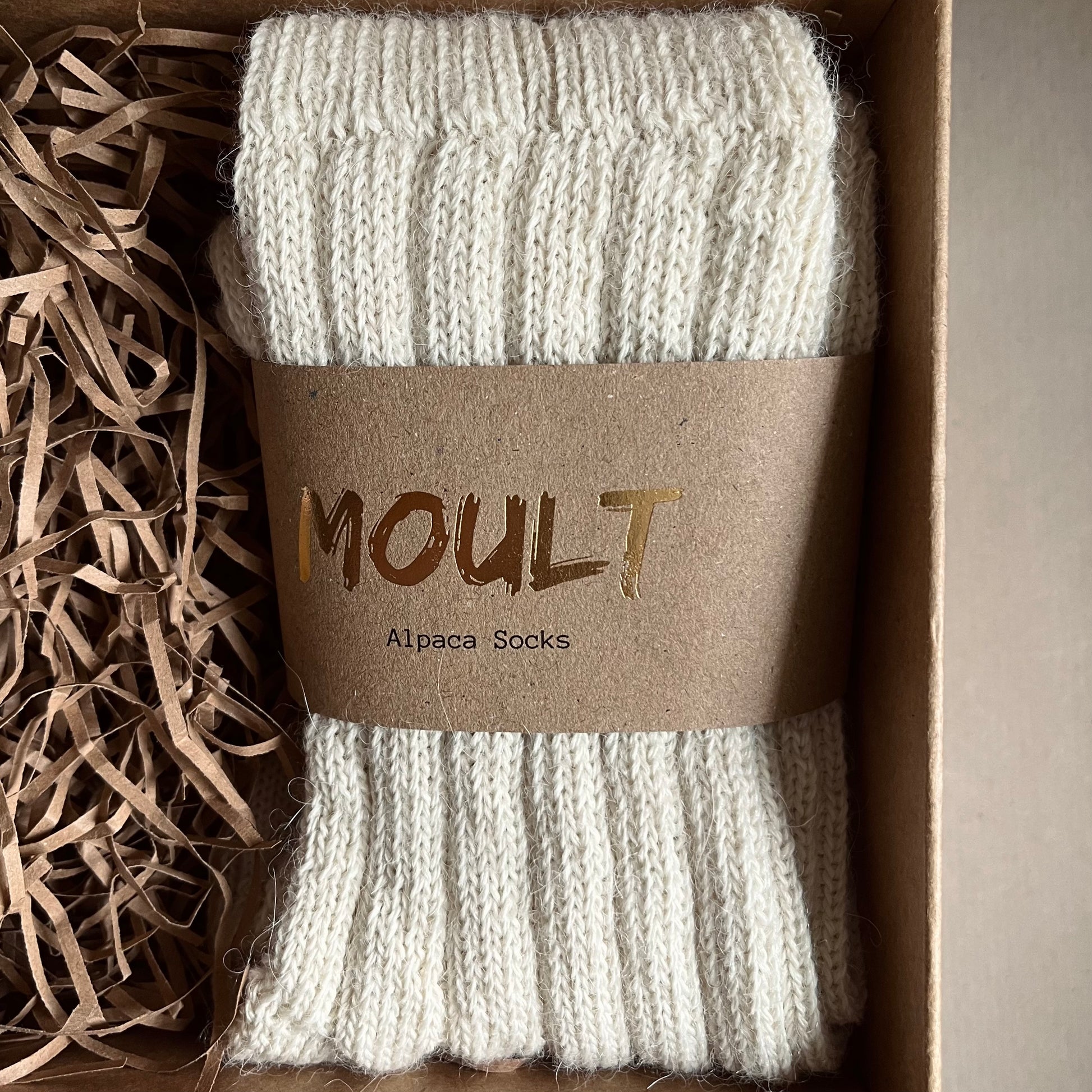 Close up image of a pair of neutral alpaca socks with a brown Kraft belly band label displaying the wording ‘Moult' included in the A Hug in a Box luxury gift box.