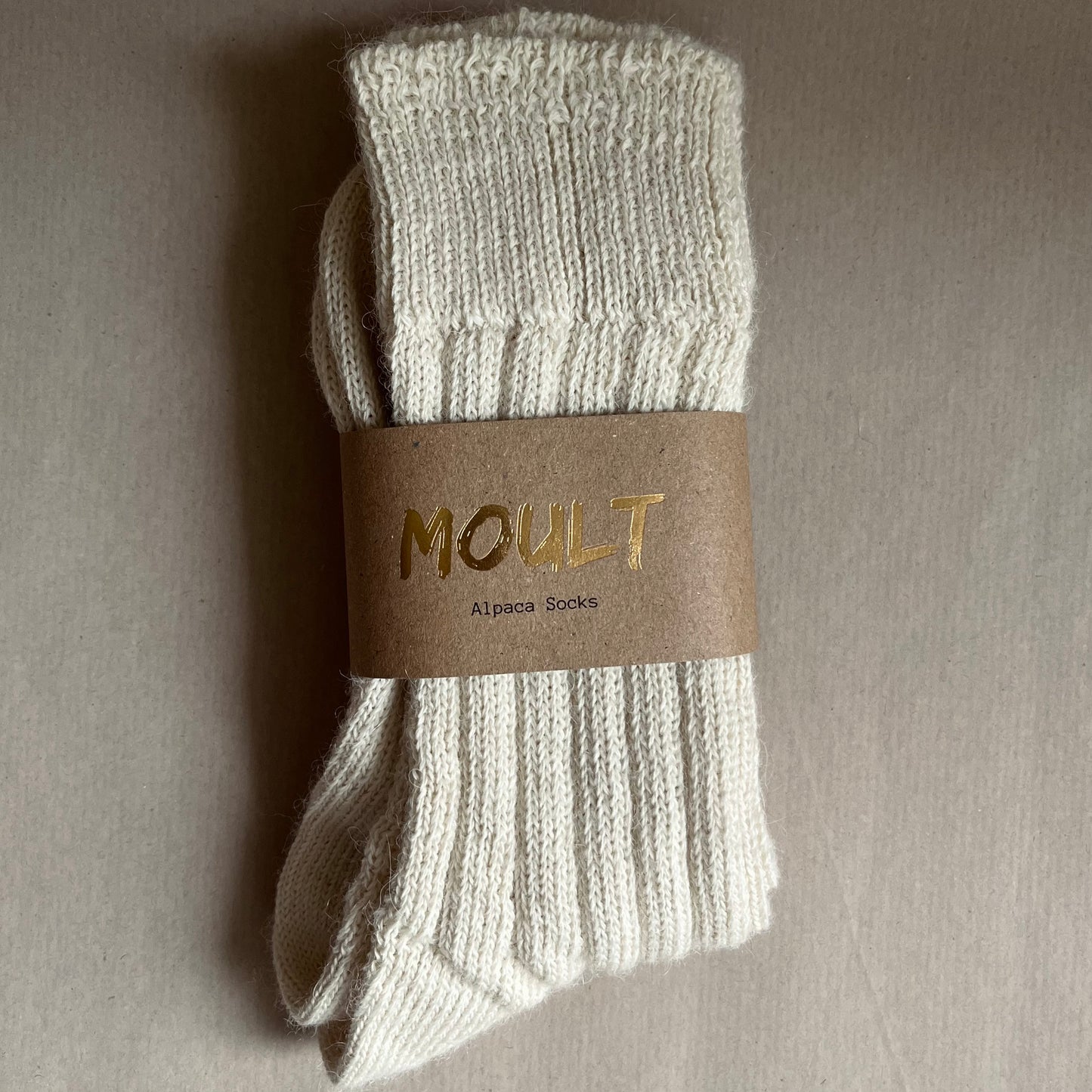 Pair of light neutral socks with a Kraft brown belly band label on a Kraft paper included in the A Hug in a Box luxury gift box.