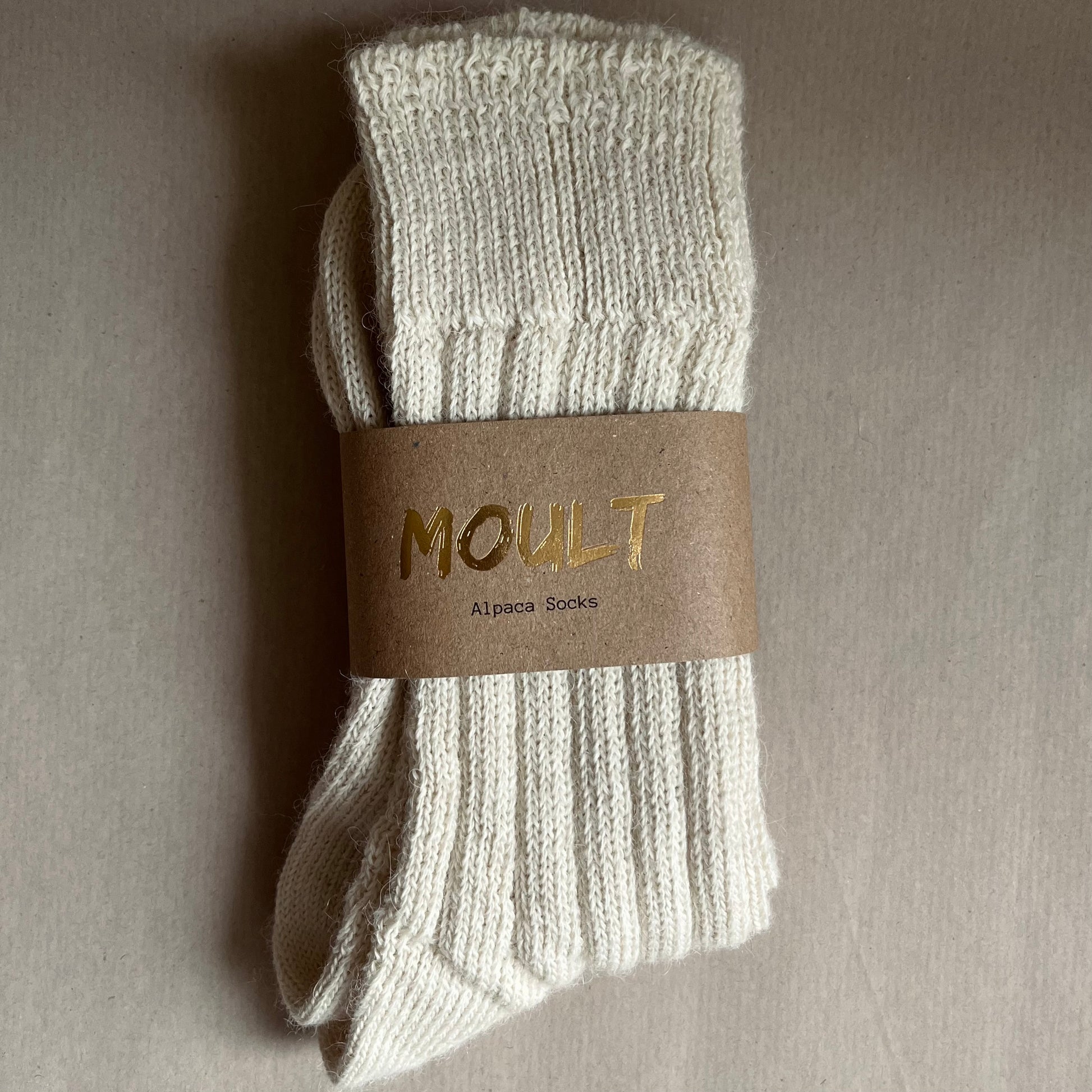 Pair of light neutral socks with a Kraft brown belly band label on a Kraft paper included in the A Hug in a Box luxury gift box.