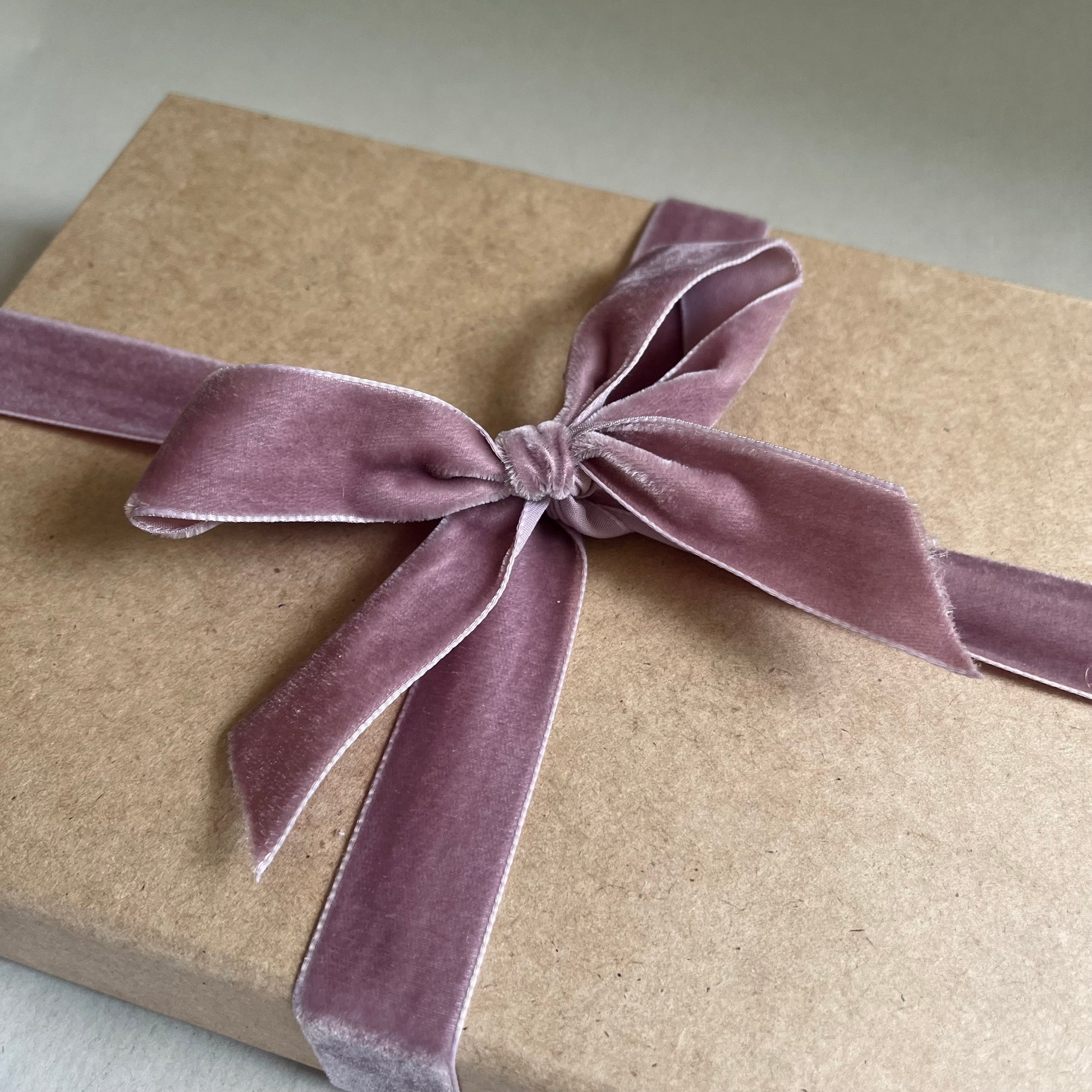 Brown kraft luxury gift box with a soft pink velvet ribbon on a neutral background